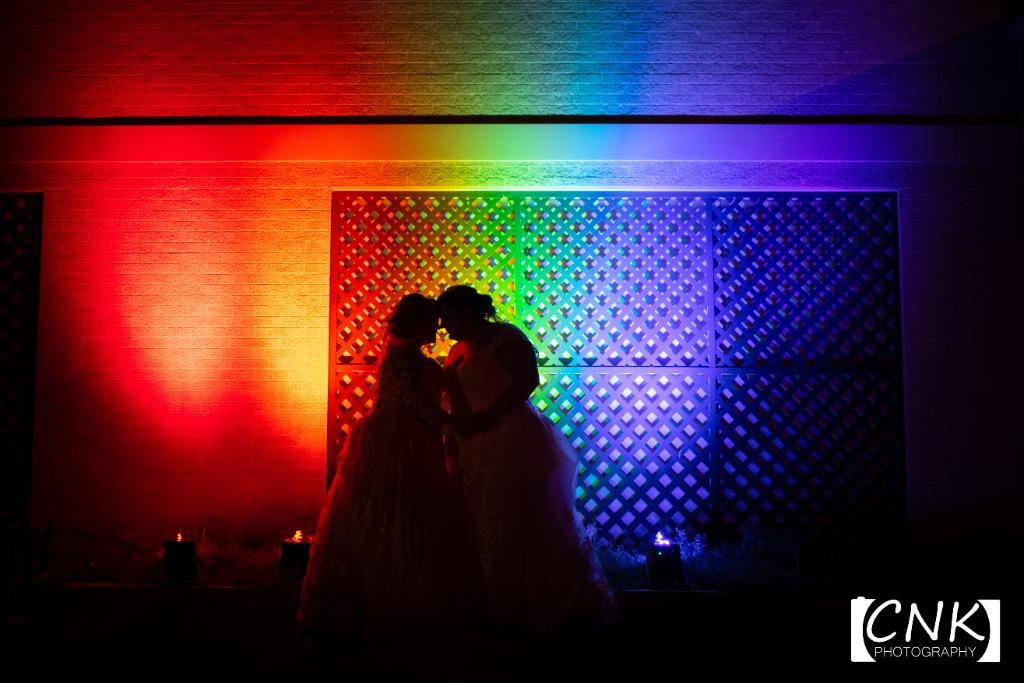 Two brides silhouetted against rainbow uplighting