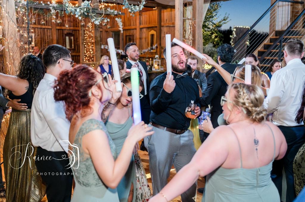 Wedding guests celebrating with glow sticks at barn reception